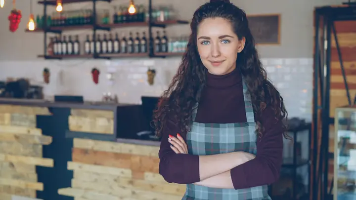 A smiling woman behind the counter of her coffee shop