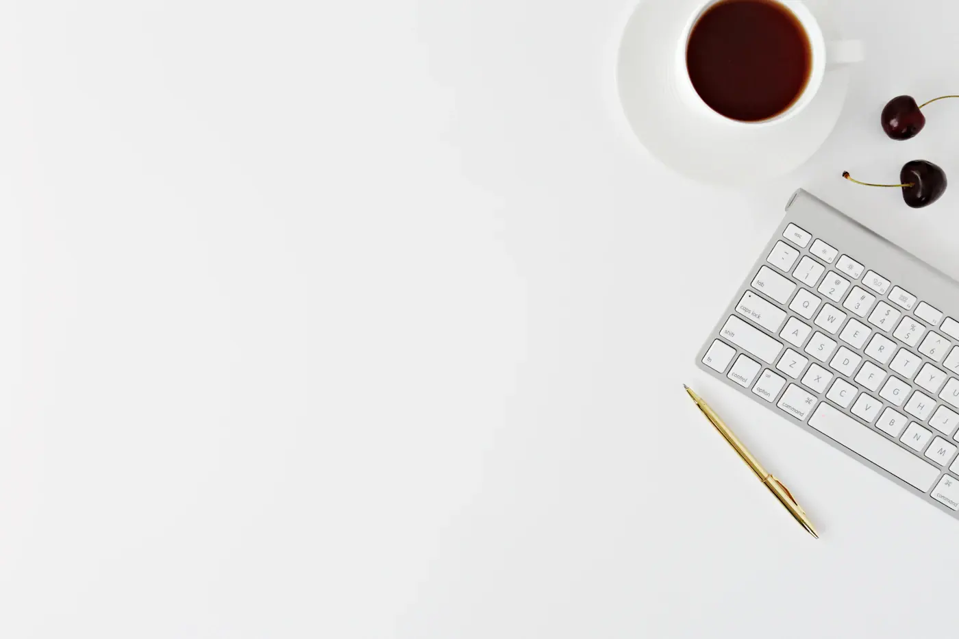 A white desk with a keyboard, a pen and a cup of coffee