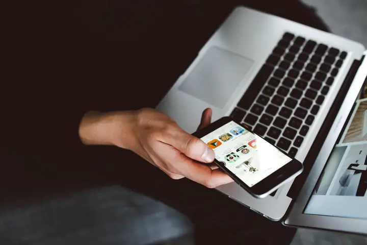 A hand holding a phone in front of an open laptop