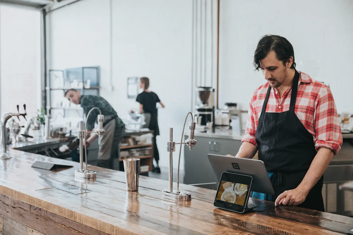 A barista in an apron using a tablet at a wooden counter